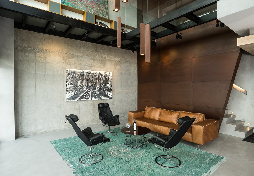 The black coffee table matches well with the three black leather chairs that stand out against the blue area rug.