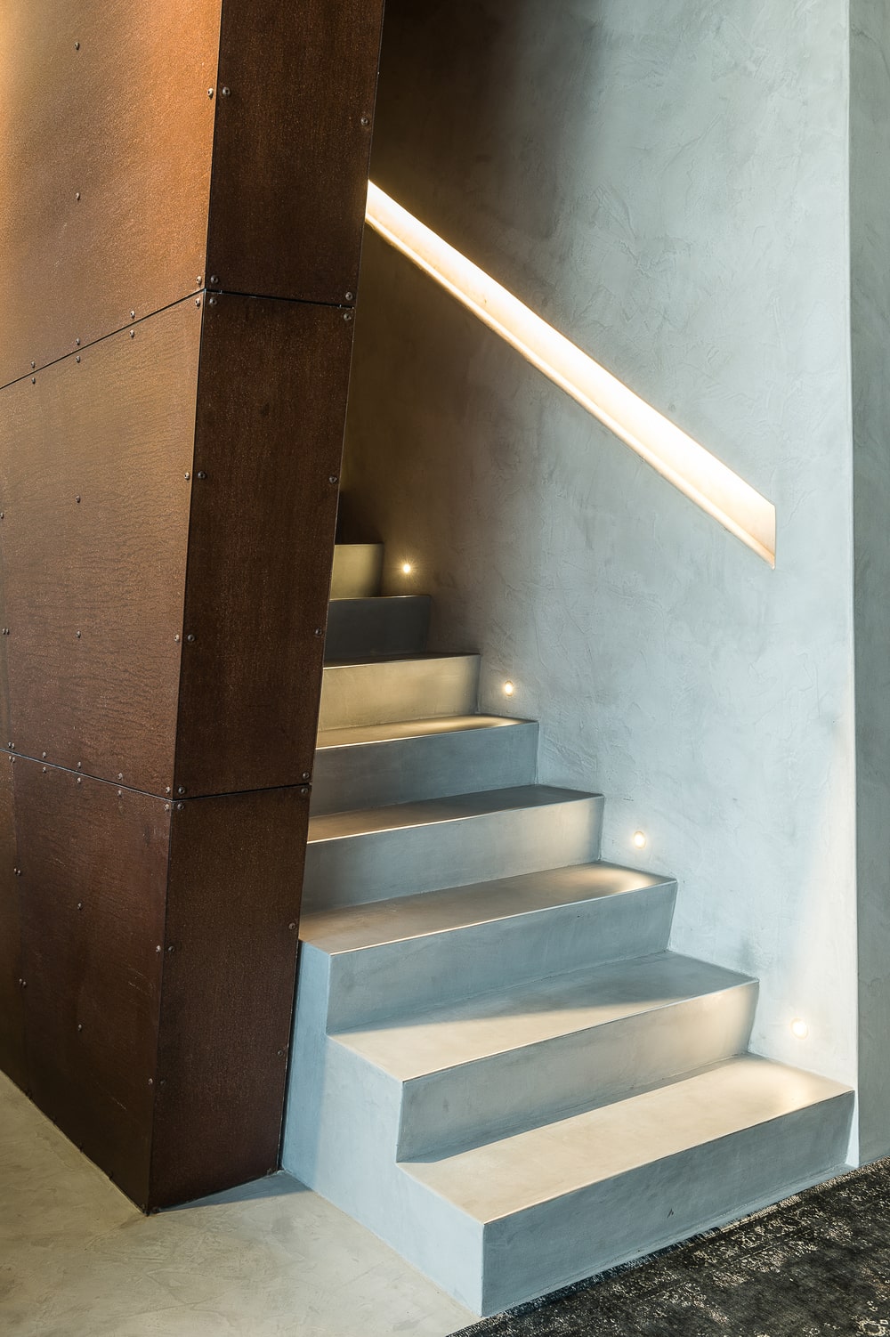 This is a close look at the staircase that has a wood paneled wall on the side and modern lighting on the other side.