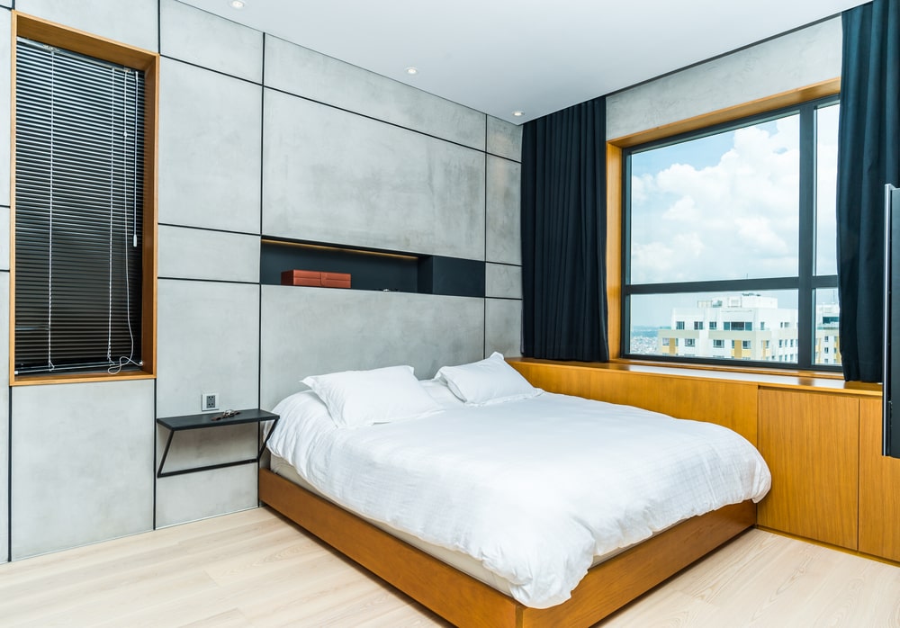 The primary bedroom has a large platform bed that is attached to the wooden cabinetry built into the wall under the window with dark curtains.