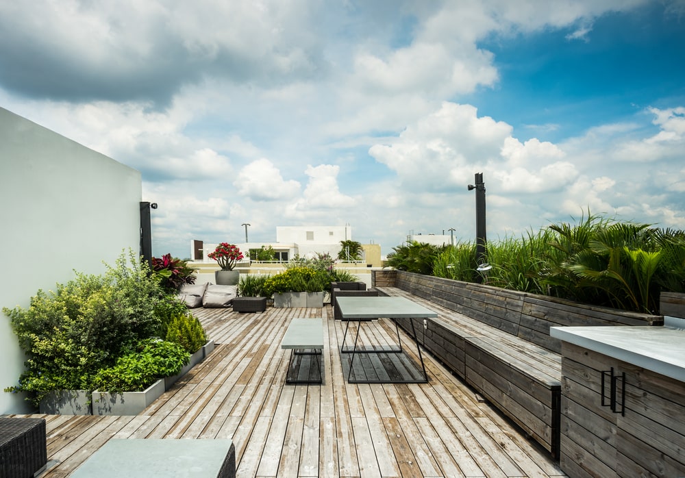 This is the rooftop patio with wooden flooring and built-in benches adorned by the various plants and shrubbery.