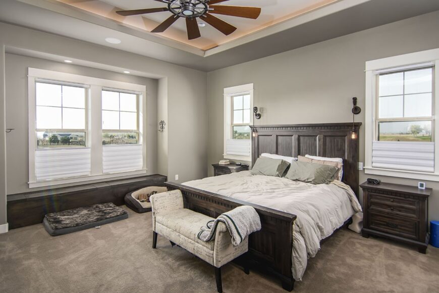 Primary bedroom with dark wood furnishings, gray walls, and a stunning tray ceiling accented with coved lighting.