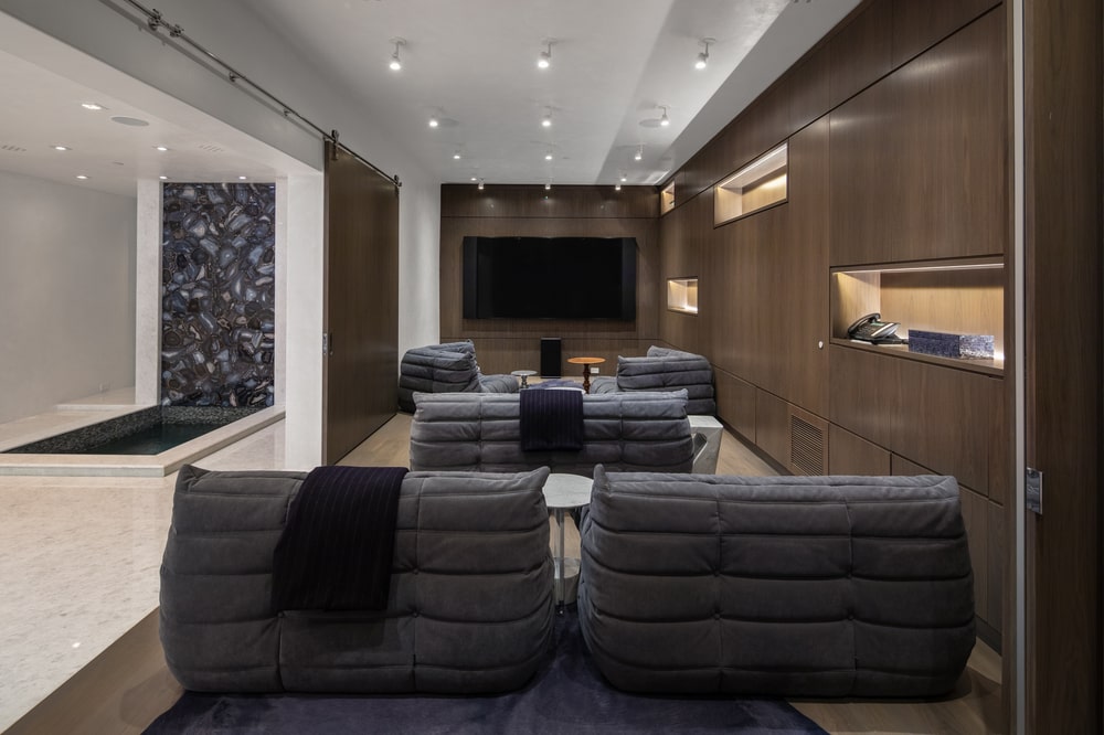 This is the den of the house with dark gray chairs, paneled walls and a wall-mounted TV on the far wall. Image courtesy of Toptenrealestatedeals.com.