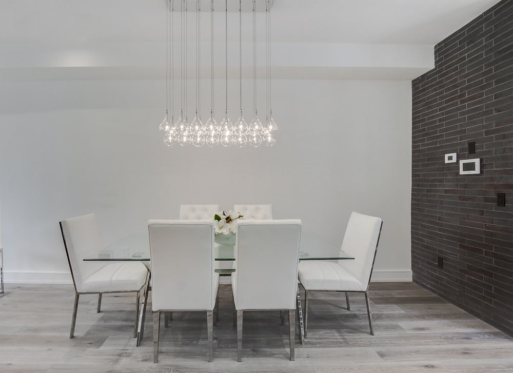 The dining area has a glass-top rectangular dining table surrounded by white modern chairs and topped with a modern decorative lighting.