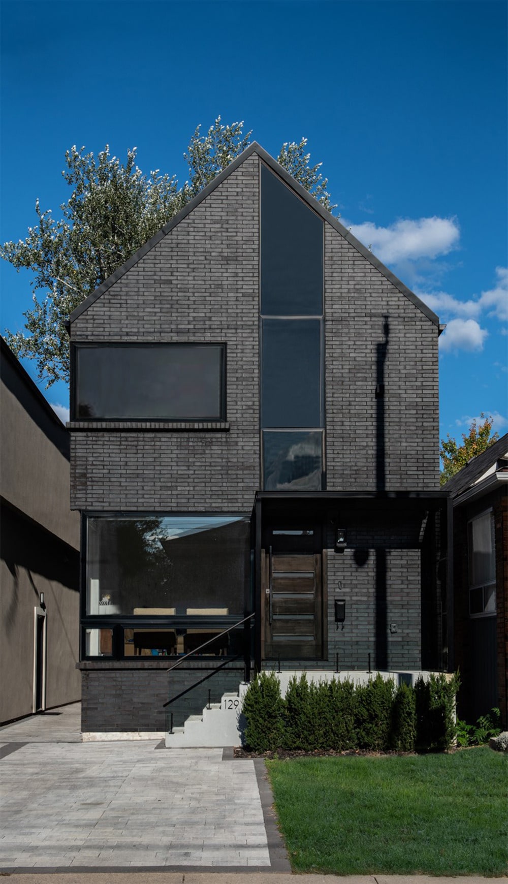 This is a view of the front of the house that has gray bricks and glass walls that give glimpses of the interiors of the house.