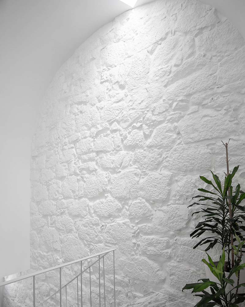 This is a close look at the wall on the side of the upper level landing that has a textured white tone with a potted plant on the side.