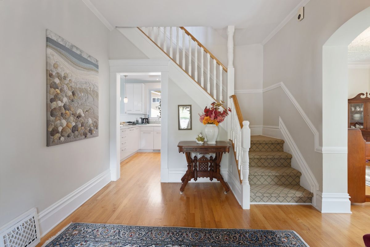 This entrance welcomes visitors with a beautiful rug on hardwood floors and a pop of color from a vase on the table next to the stairs.