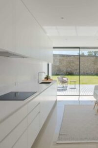 The floors and walls blend into the stark white cabinets in this bright and airy minimal kitchen.