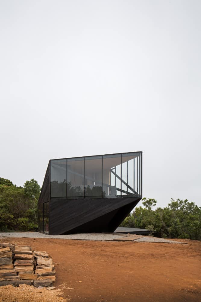 This is a view of the house with a modern design to its glass and black exteriors that make it stand out against the surrounding landscape.