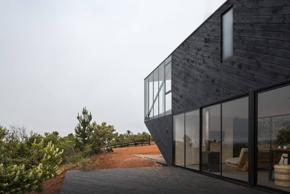 This is a closer look at the side of the house with glass sliding doors and glass windows above that stand out against the dark exterior walls.