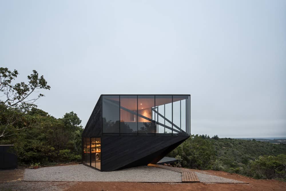 This is an exterior view of the side of the house with a black exterior look to it complemented by the surrounding landscape that has graveled soil and wooden walkway.