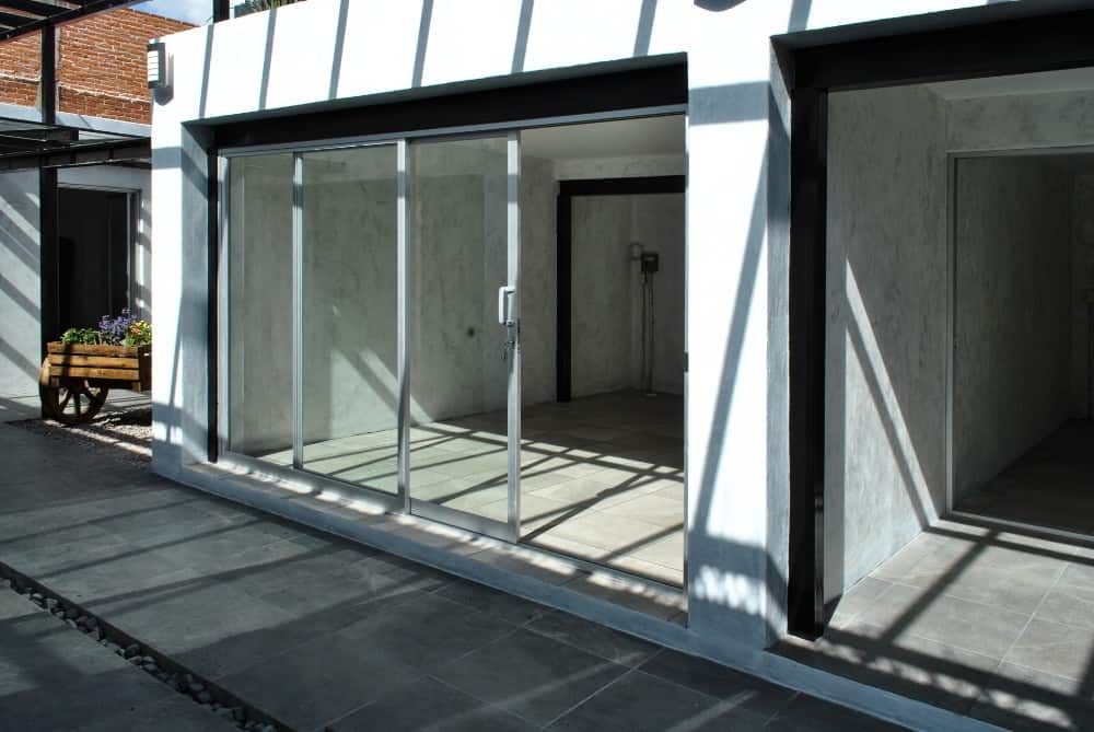 This is a close look at one of the sliding glass doors that open to a large concrete room with gray flooring tiles and an abundance of natural lighting.