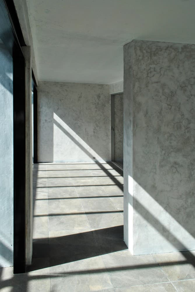 This is an interior view of the house showcasing the spacious and bright room with concrete walls and gray flooring tiles.