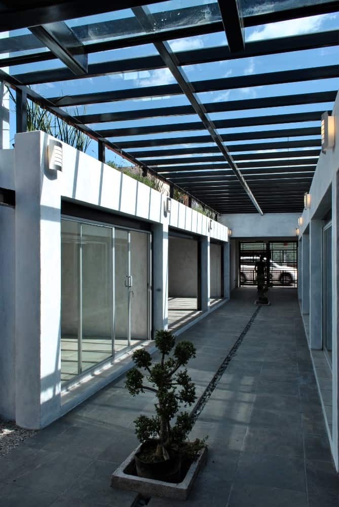 This is a full view of the interior courtyard of the house with potted plants, concrete walkway and glass ceiling with dark metal beams.