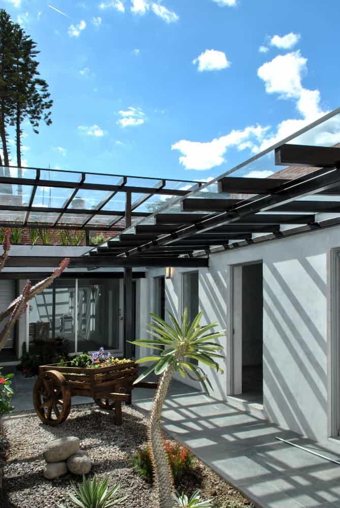 This is a view of the house exterior from the vantage of the garden showcasing the metal beams of the glass ceiling and the trellises.