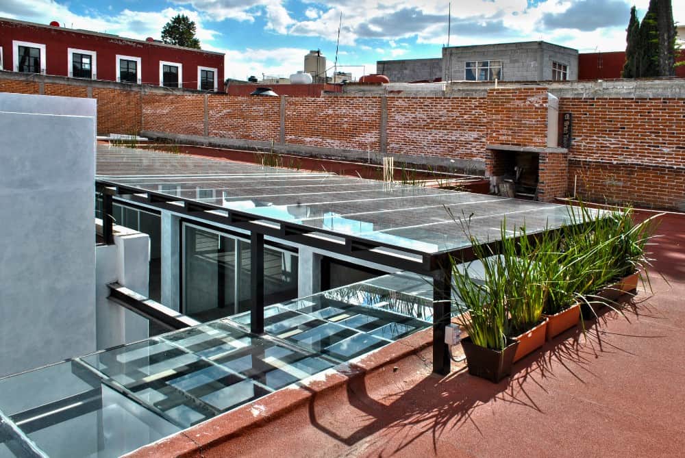 This is a view of the house from the vantage of the rooftop that has a terracotta flooring and planters with a view of the glass ceiling over the courtyard.