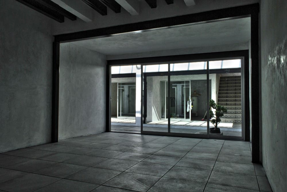 This is a view of the interior of the house with a spacious room that has concrete walls, a beamed ceiling and gray flooring tiles.