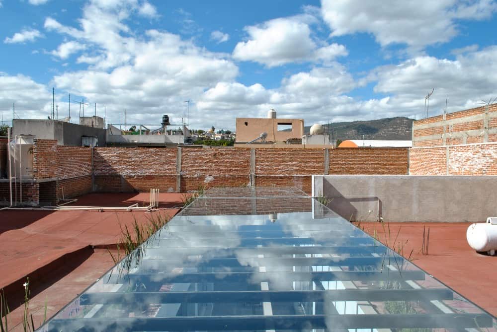 This is a close look at the glass ceiling above the courtyard supported by beams of metal with a view of the rooftops that have terracotta floors.