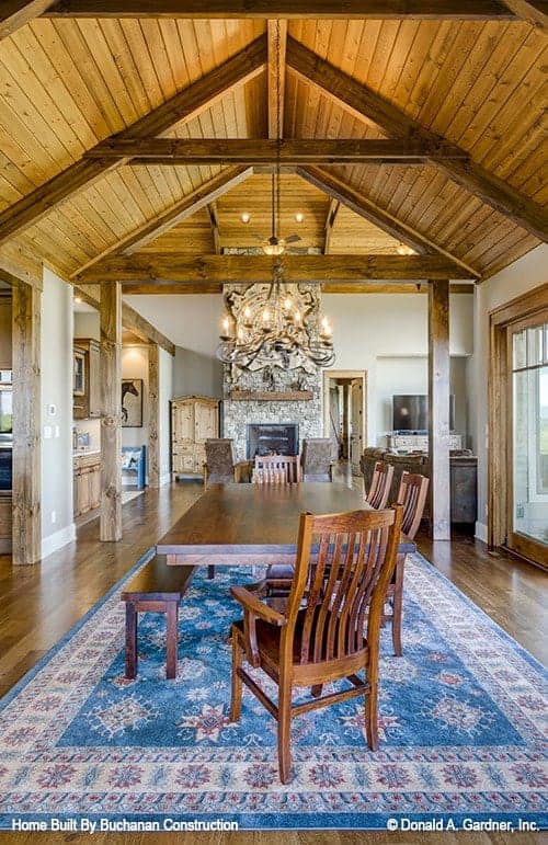 The simple dining area is a few steps from the living room with a view of the fireplace. It has a rectangular wooden dining table paired with a wooden bench and wooden chairs on a colorful patterned area rug.