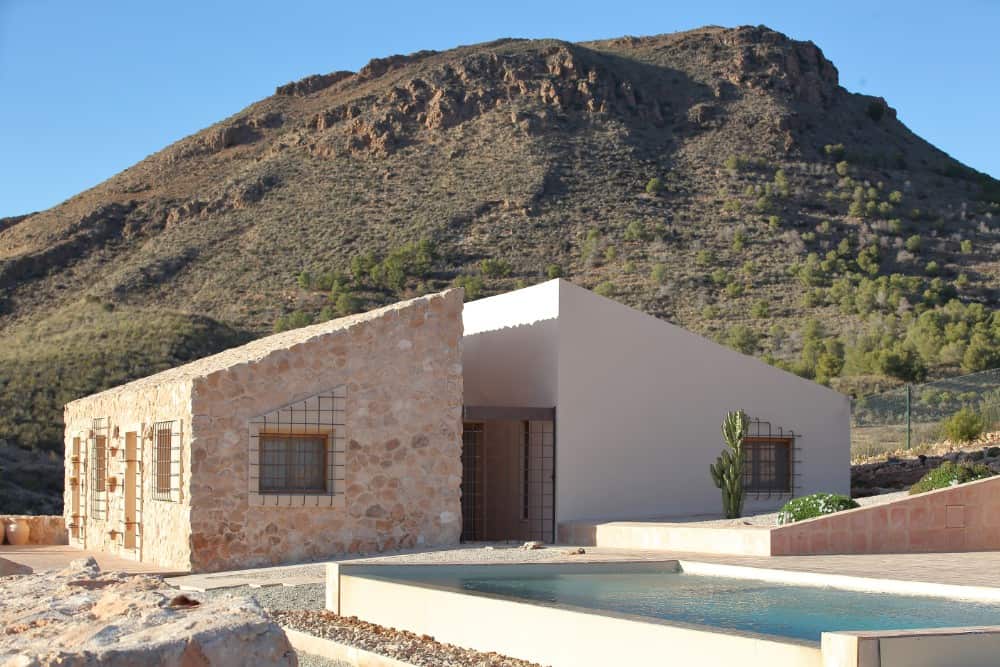 This is an exterior view of the stone house that matches its tone with the surrounding landscape.