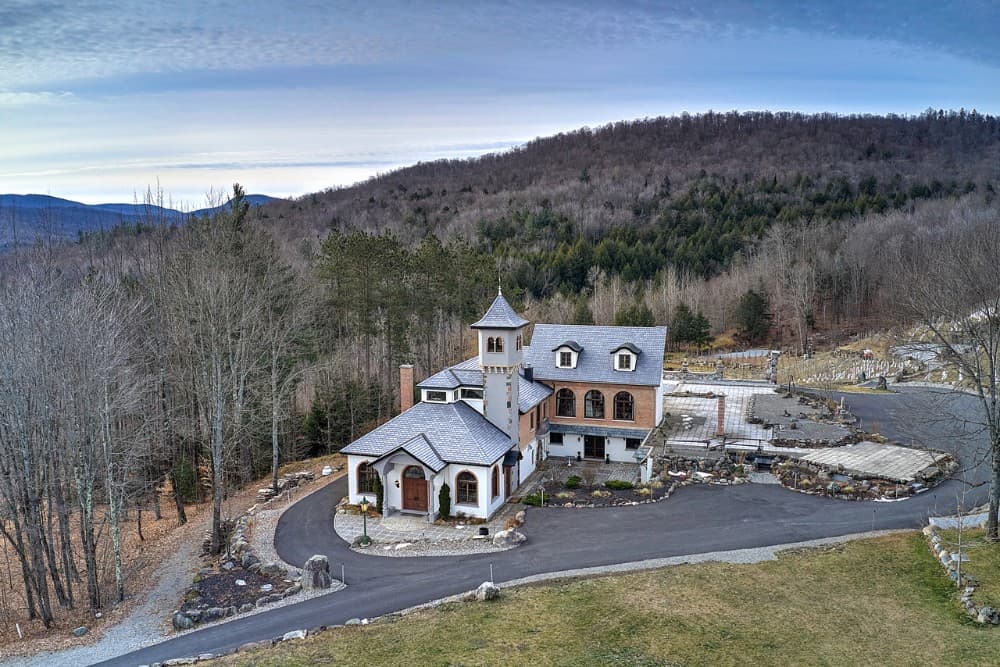 The renovated house has a stucco exterior, arched windows, gable dormers, and a turret. Image courtesy of Toptenrealestatedeals.com.