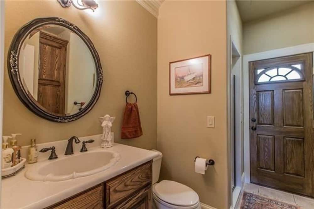 Bathroom with a single-sink vanity, a toilet, and beige walls adorned with a round mirror and framed artwork.