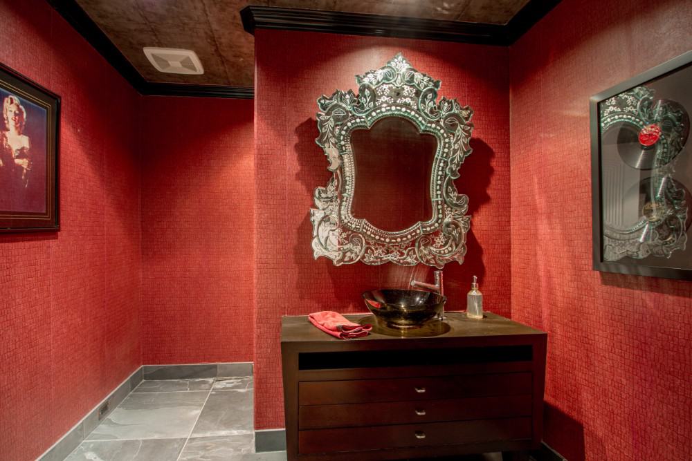 Powder room with a vessel sink vanity and bold red walls adorned with an intricate mirror and framed artworks. Image courtesy of Toptenrealestatedeals.com