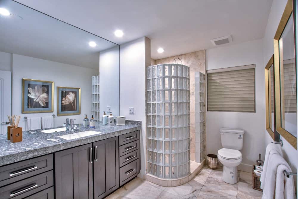 Bathroom with a large vanity, a toilet, and a walk-in shower encased in curved glass blocks.