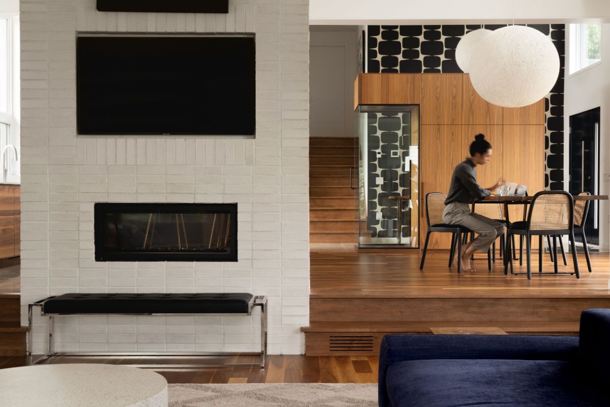 Living space with bricks wall fireplace, connected to dining area in wooden design.