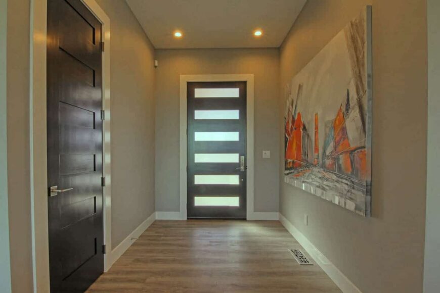 The foyer has a glazed front door and a large painting that adorns the gray walls.