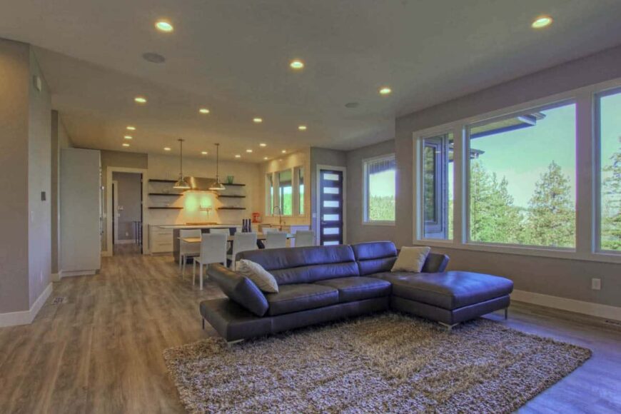 An open layout view of the great room, dining area, and kitchen well-lit by recessed ceiling lights.