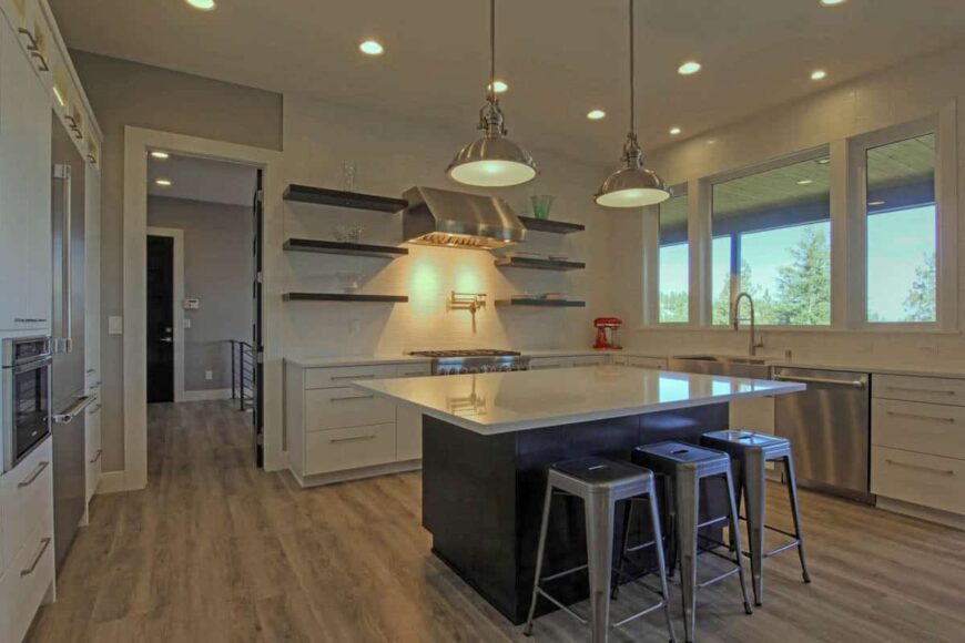 The kitchen is equipped with stainless steel appliances, white cabinets, floating shelves, and a breakfast island.