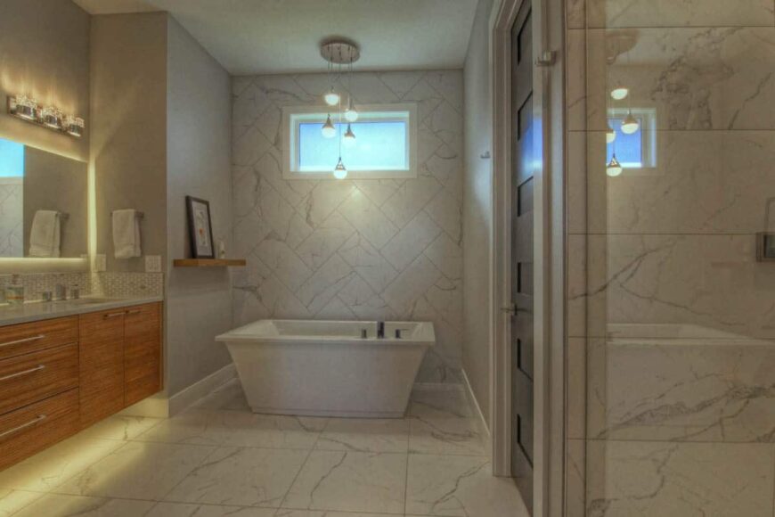 The primary bathroom has a marble tiled floor, a wooden vanity, and a freestanding tub topped with cascading pendants.