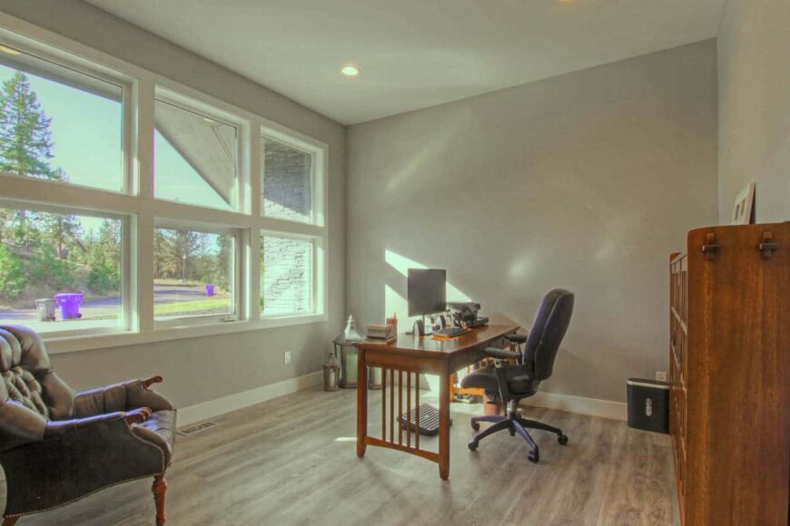 Home office with a wooden desk, leather seats, and plenty of windows overlooking the front yard.