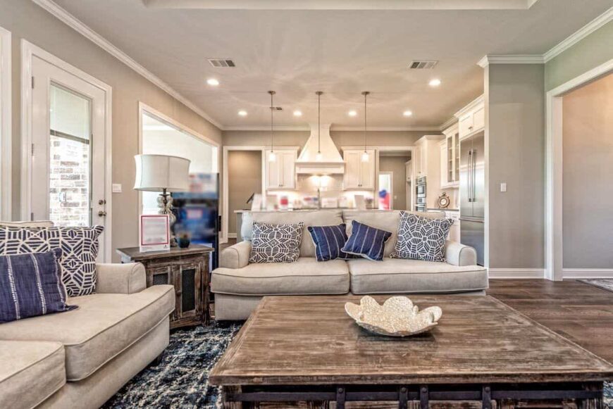 A large, wooden coffee table complements the beige sectional sofas.