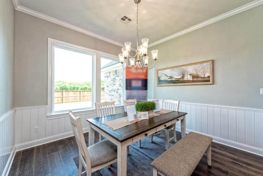 The dining area has a rustic dining set and gray walls adorned with half beadboard and a landscape painting.