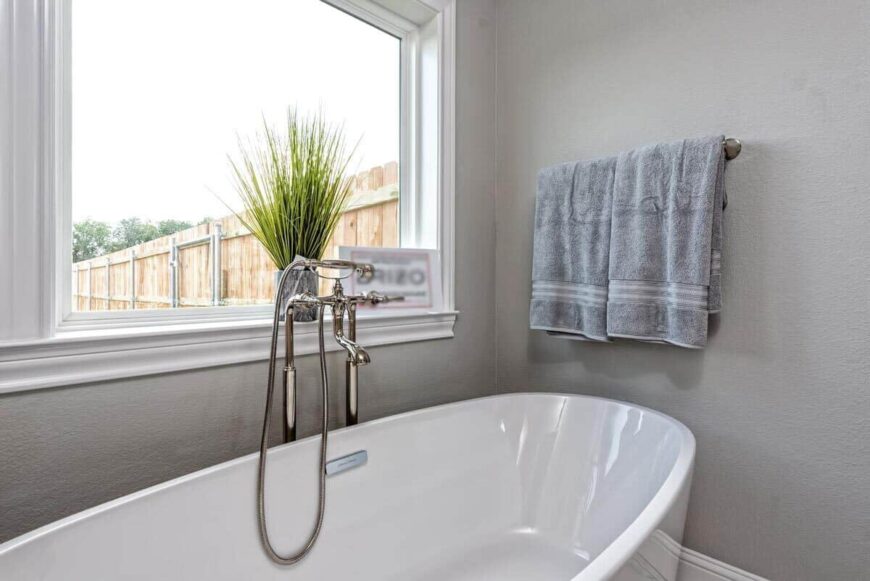 A picture window adorned with a potted plant brightens the freestanding tub.