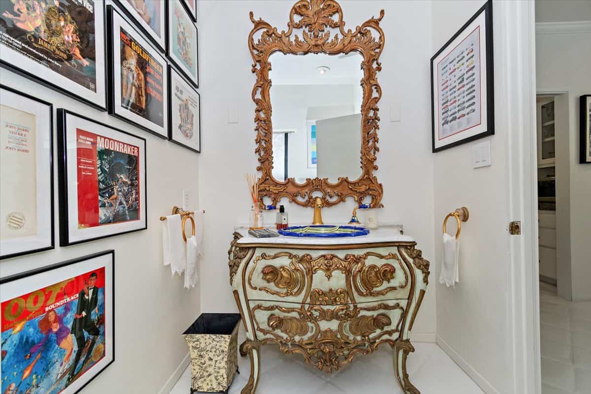 The powder room is filled with a gallery of posters and an intricate vanity with a carved wood mirror. Image courtesy of Toptenrealestatedeals.com.