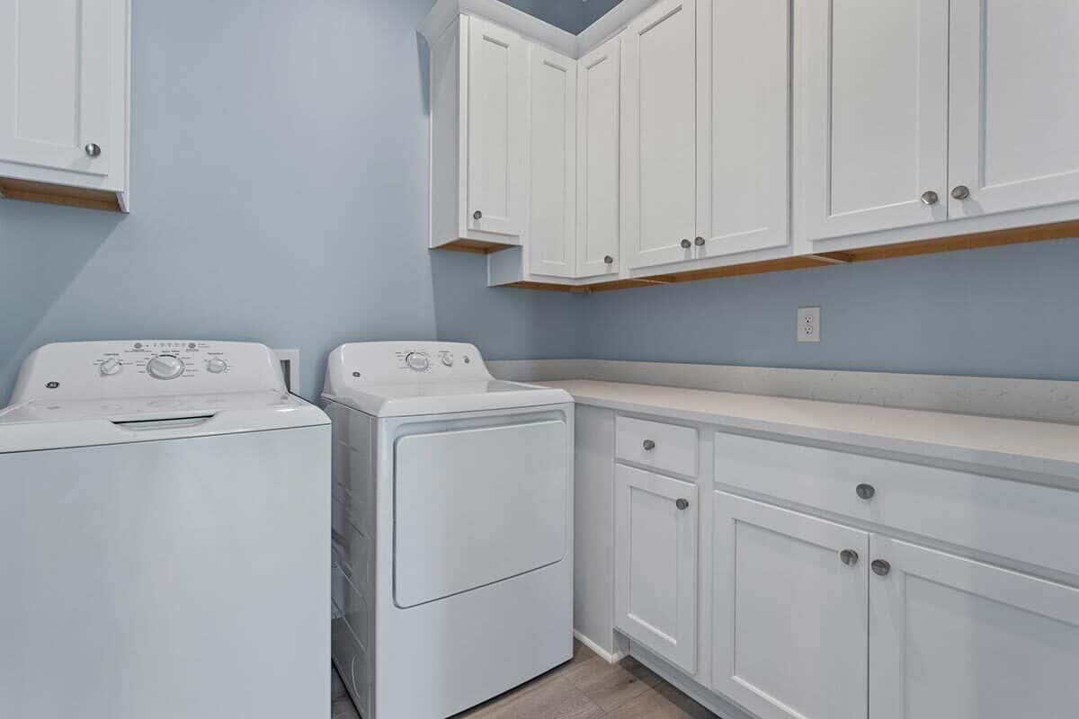 The laundry room has plenty of cabinets, a white washer and dryer, and quartz counters.