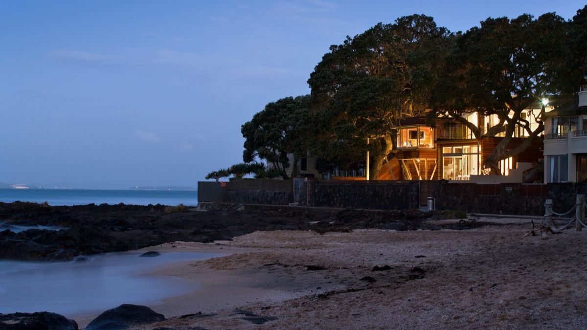 A scenic photograph taken from the shoreline, showcasing Thorne Bay House from a distance as the sun sets.