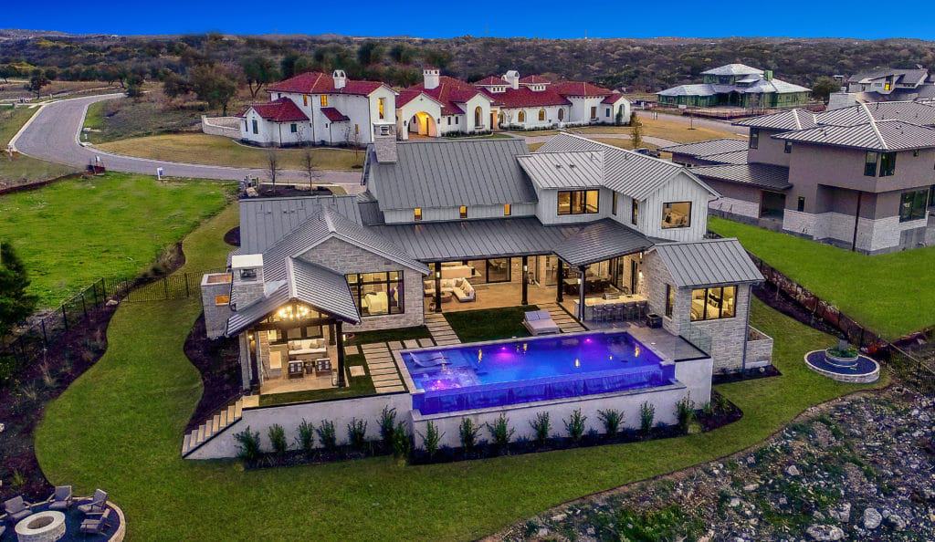 Aerial view of the Hill Country Farmhouse showcasing its expansive outdoor spaces and illuminating pool.