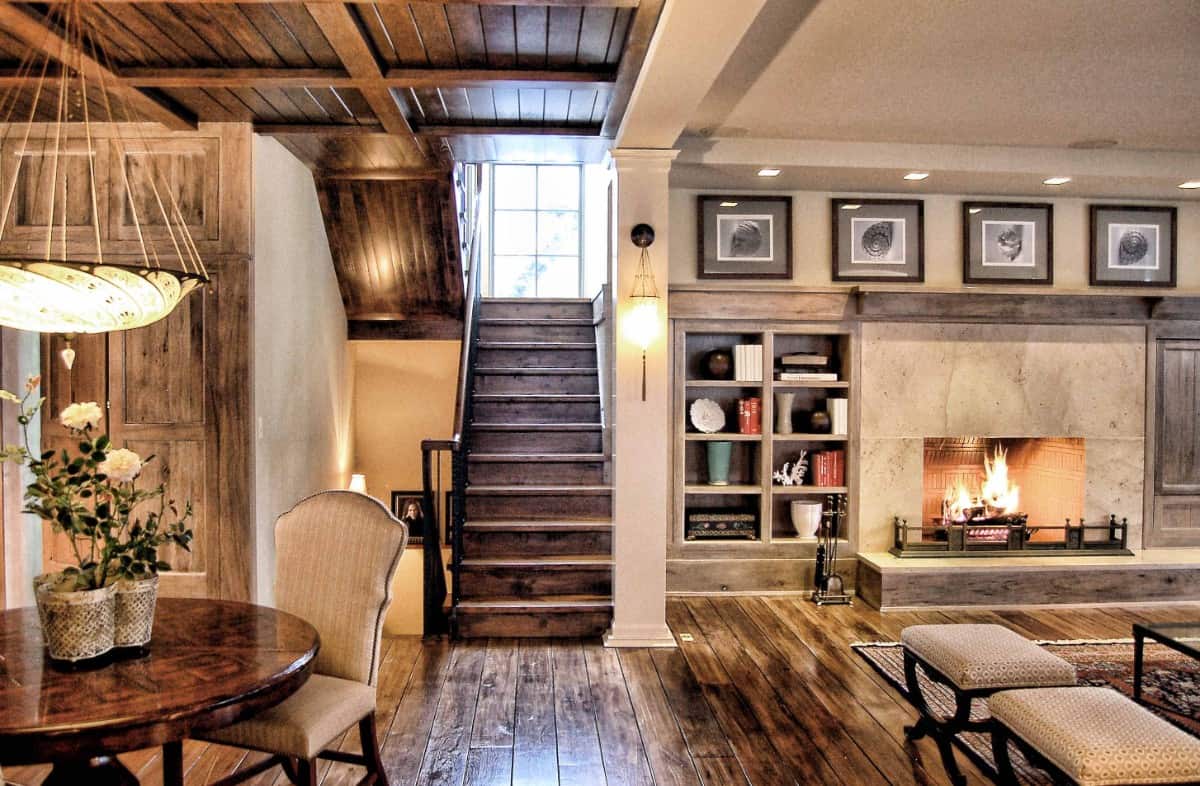 An open living space with beige walls and wide plank flooring that matches the stairs and coffered ceiling above the dining area.