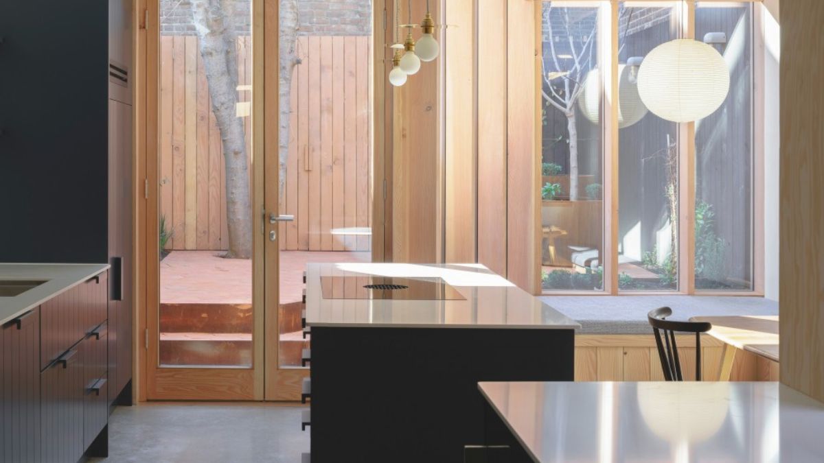 A picture of a spotless kitchen with high glass doors and deep-framed timber windows that let in natural light.