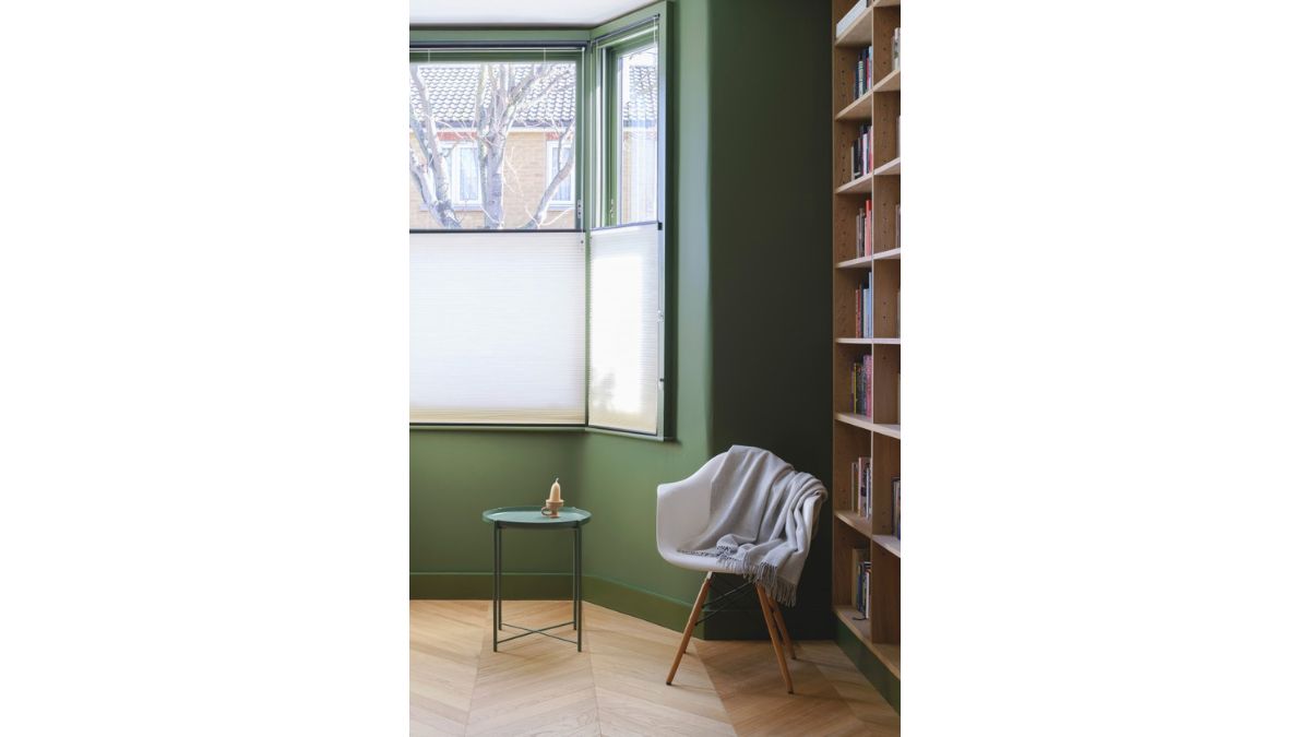 A pleasant upper floor room with a green wall, a spotless wooden floor, and book shelves.