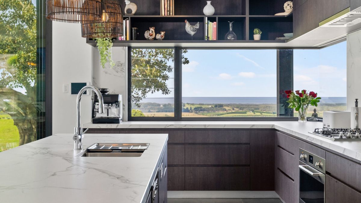 The kitchen features a detailed design, with a wide glass window that floods the space with natural light and offers panoramic views of the surrounding landscape. 