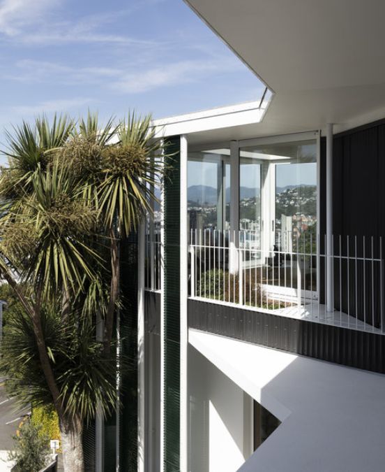 Exterior photograph of the second floor of Salmont Place showcasing a room with open sliding glass door leading to a veranda enclosed by white fence, surrounded by trees that blend with the building's aesthetic.