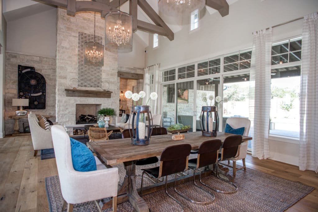 Combined living room and dining area with a brick fireplace and a cathedral ceiling adorned with exposed trusses and elegant drum chandeliers.