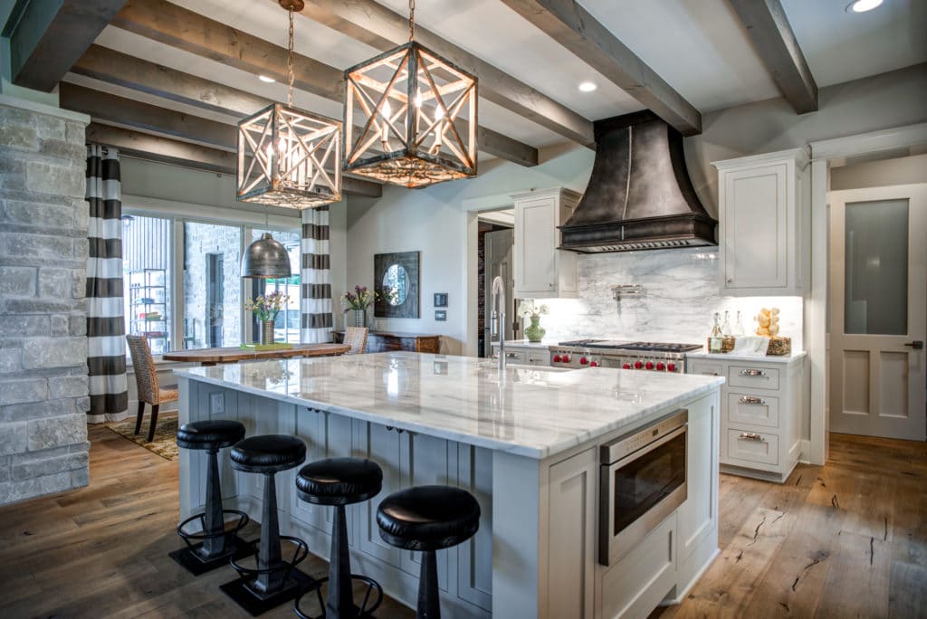 The kitchen features a beamed ceiling and a large island topped with caged pendants.