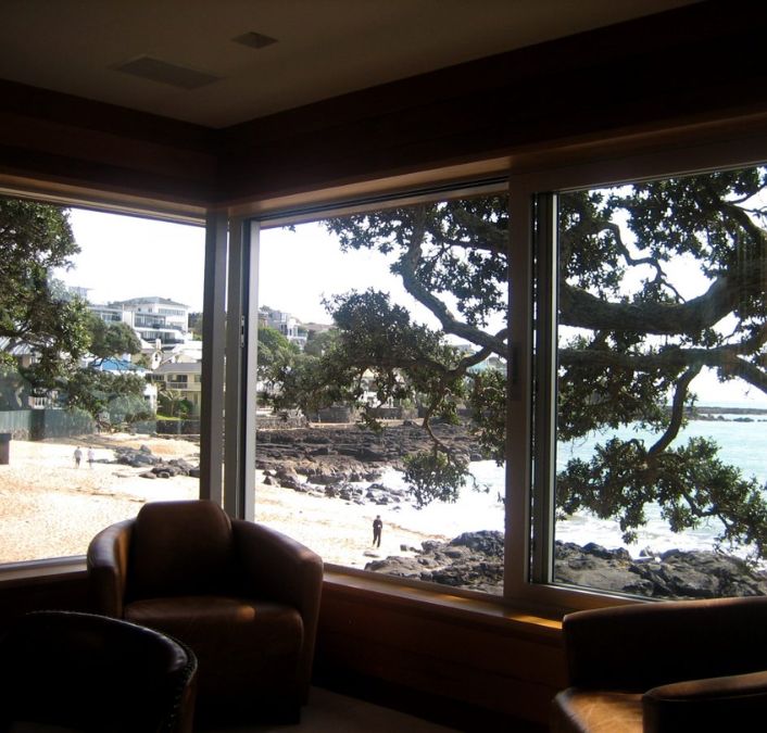 An interior shot of a room with sliding glass windows that showcase a panoramic view of the shoreline with much solid volcanic rock outside the house.