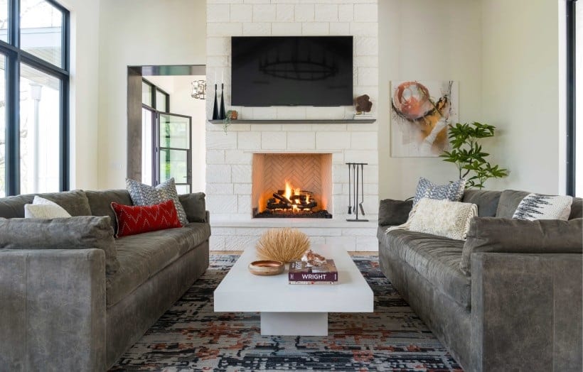 The stone fireplace with a TV on top is mirrored in the living room. It includes facing velvet sofas and a modern coffee table.