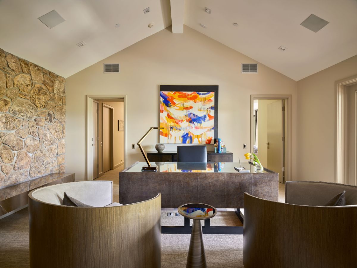 A bright home office with a vaulted ceiling, stonework walls, and wall arts. Image courtesy of Toptenrealestatedeals.com